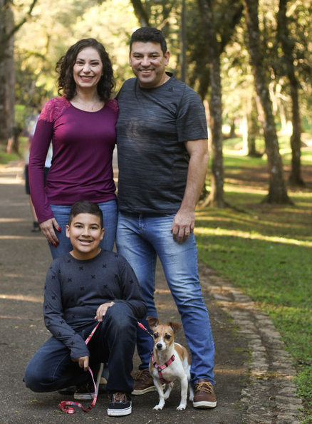 Photo of a mother, father, boy, and small dog, outdoors on a path and posing for a photo.