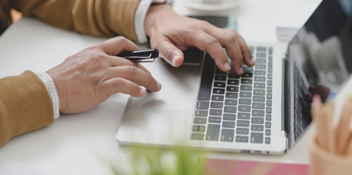 Hands of a man working on a laptop; perhaps to calculate cash value of his life insurance