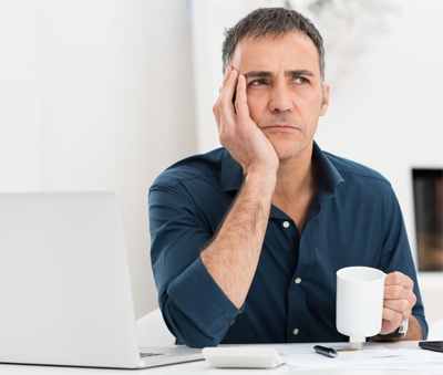 Middle-aged man sittiing at a computer and thinking - perhaps about private vs employer life insurance
