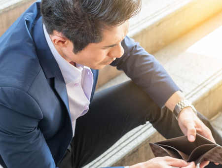 Man sitting on steps and looking into his wallet - for information on how to stop ruining your financial future